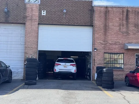 An SUV parked inside an open workshop bay with stacks of tires either side of the doorway.