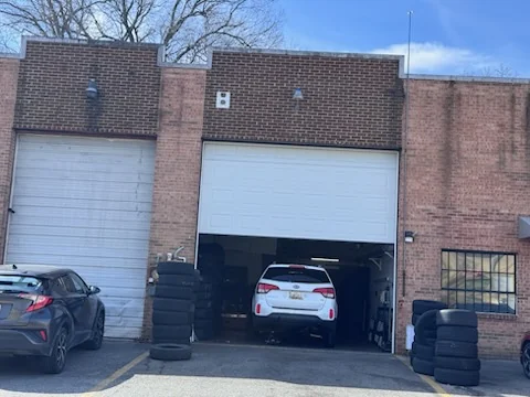 A brick unit with a roll-up bay door raised, a car inside and stacks of tires beside the entrance.