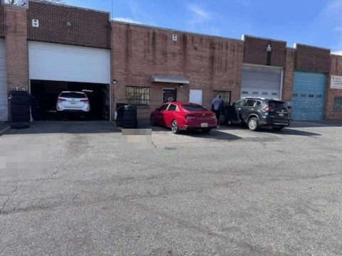 Two open workshop bays along the front of a brick unit with customer cars parked outside.