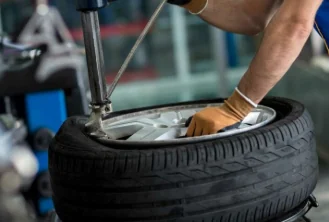 Gloved hands working a tire onto a rim on a fitting machine.