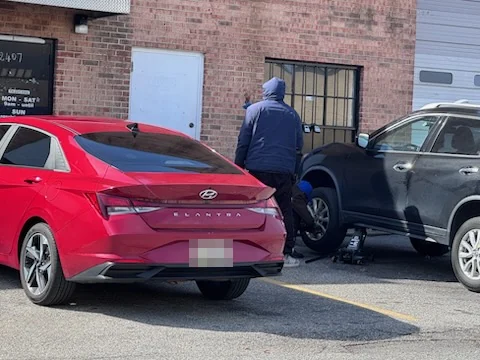 A person working on a vehicle at the front of the shop, beside a red sedan.